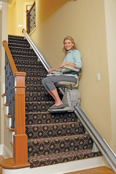 Mujer sonriendo mientras utiliza una silla salvaescaleras recta en la escalera de su hogar